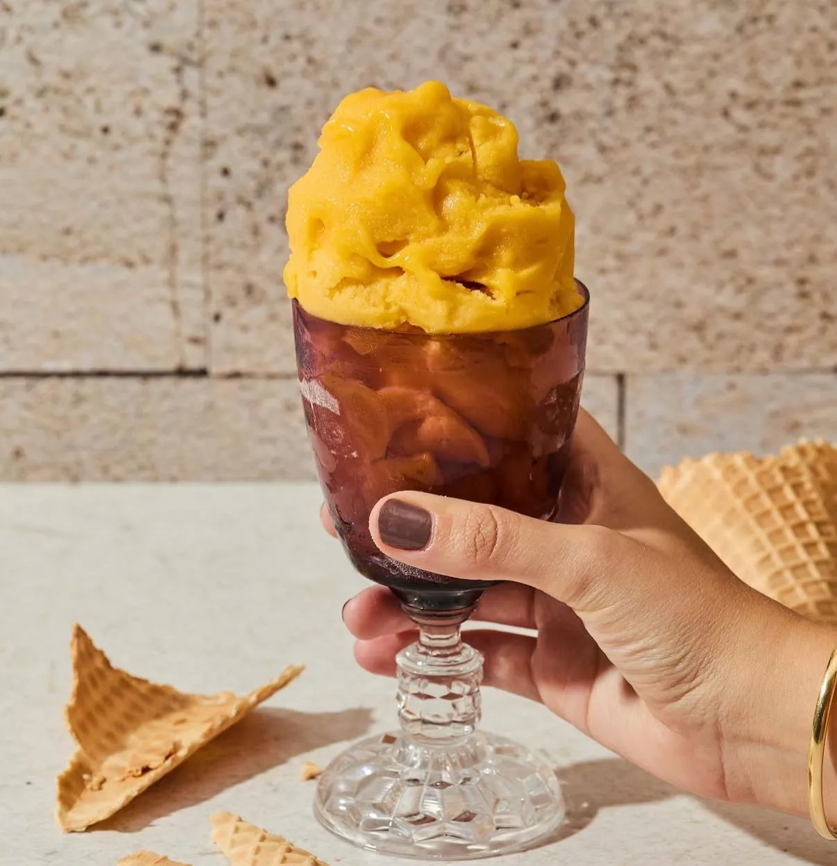 Copa de sorbete de maracuyá y mango sostenida en una mano, con trozos de cono de barquillo alrededor