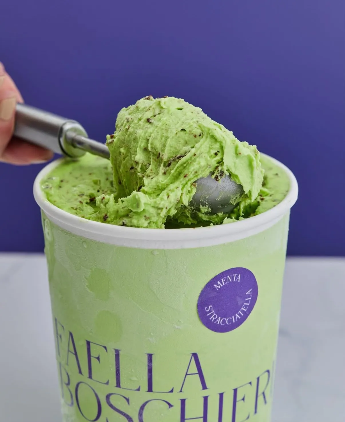 Pote de gelato de menta stracciatella con virutas de chocolate, siendo servido con una cuchara de helado