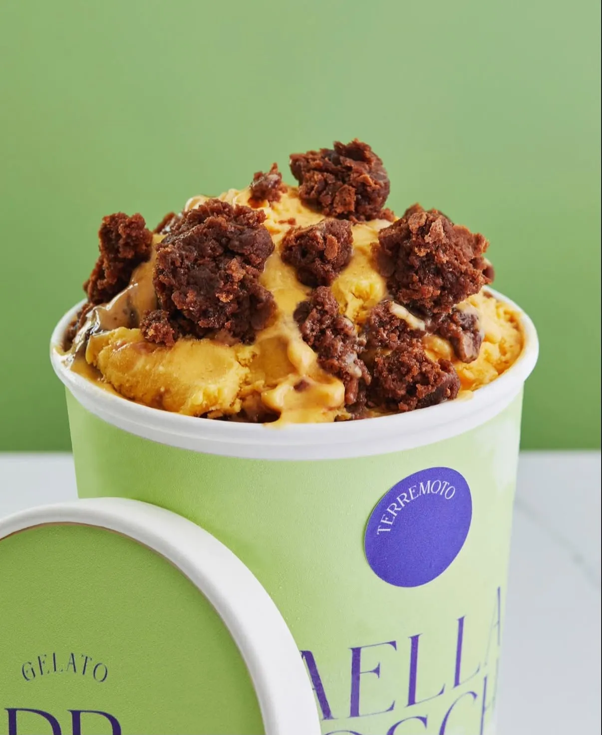 Pote de gelato de lúcuma cubierto con trozos de brownie y fudge de olla