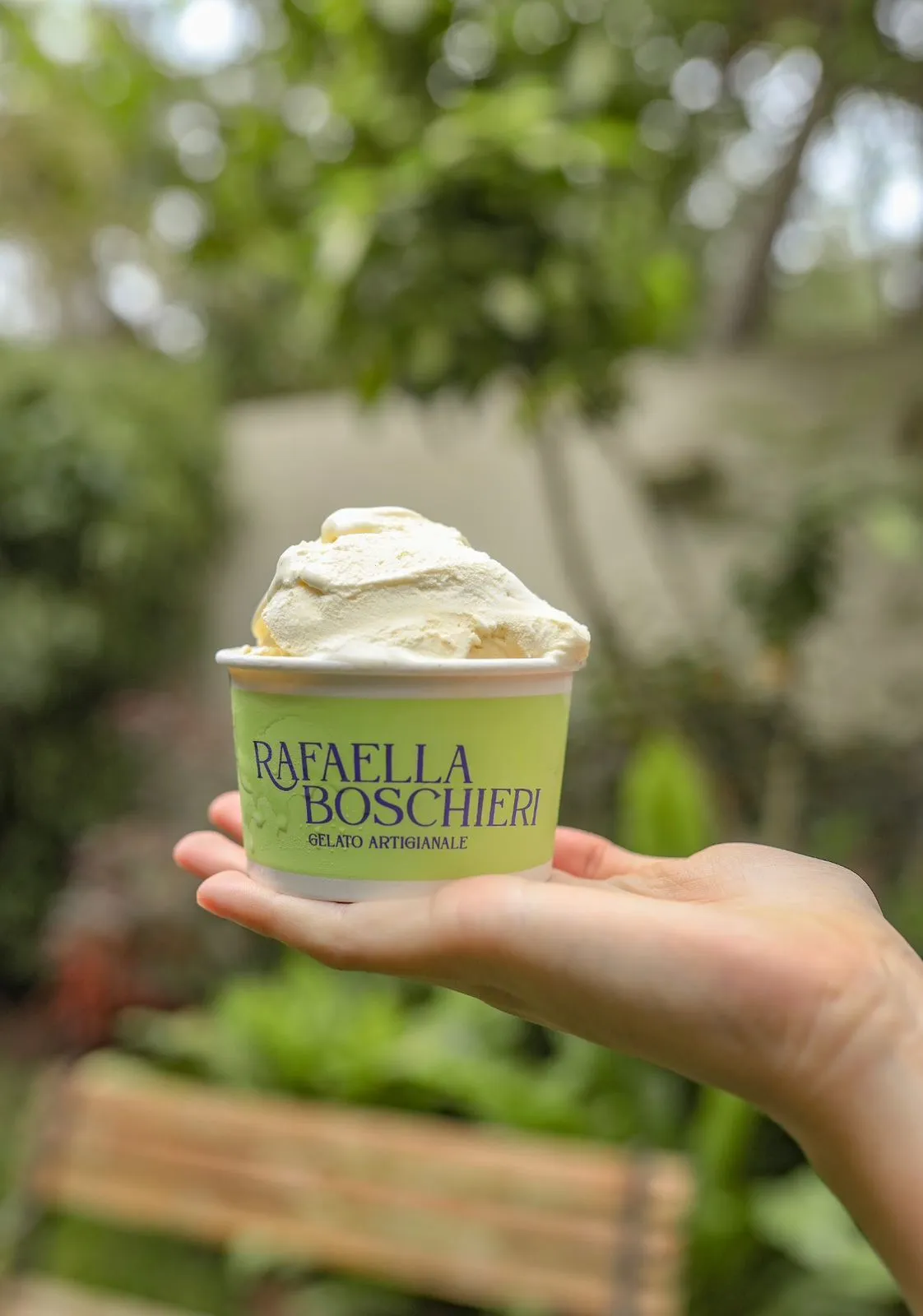 Pote de gelato de vainilla sostenido con la mano en un jardín